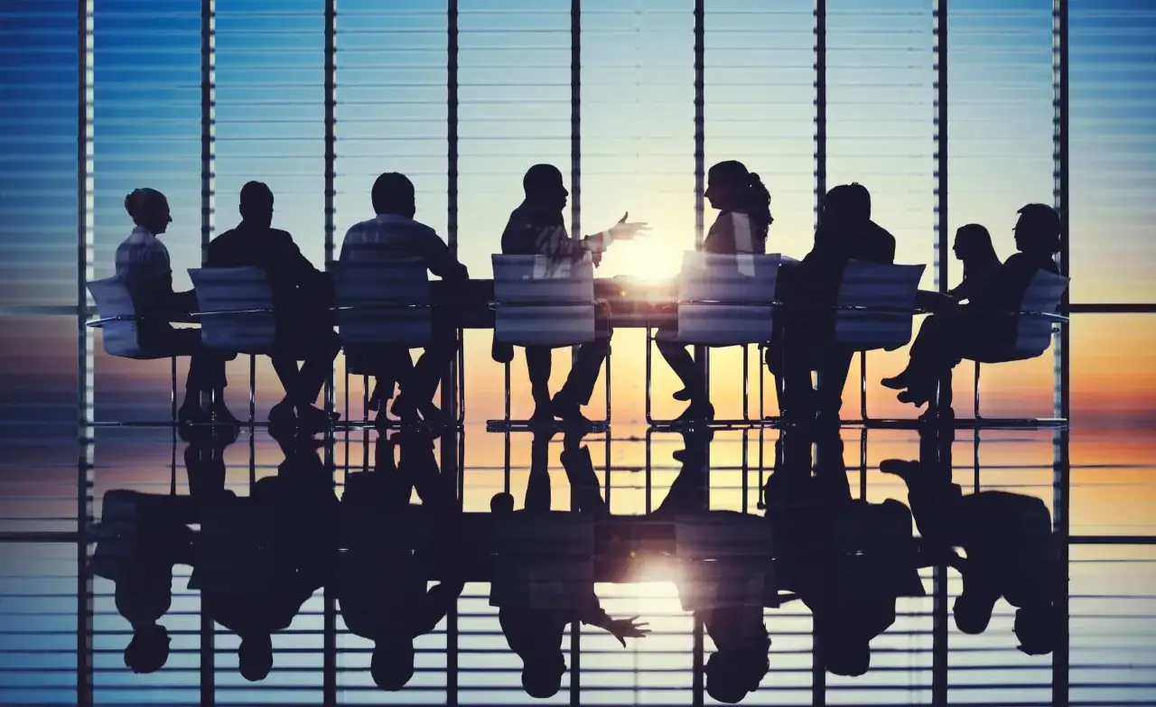 Silhouettes of people in a meeting room, reflecting on a polished floor, showcasing active board engagement during a sunset.