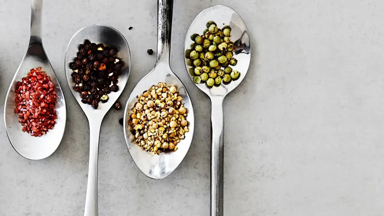 Fyra skedar med olika peppar sorter: röd, svart, gul och grön. En visuell resa genom pepparns värld.