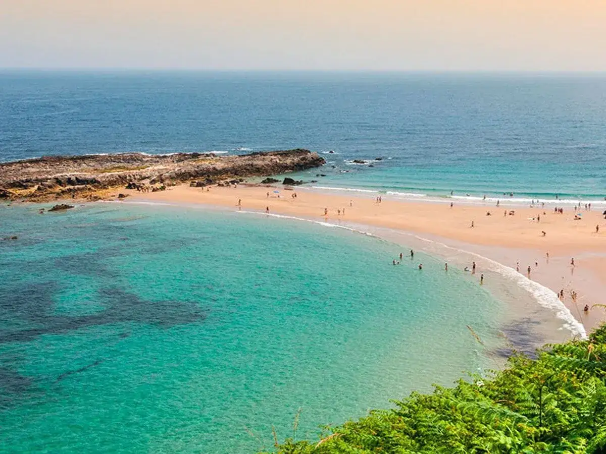La **playa de la rabia** se extiende con arena dorada y aguas turquesas. Personas disfrutan del sol y el mar en este idílico paisaje costero.