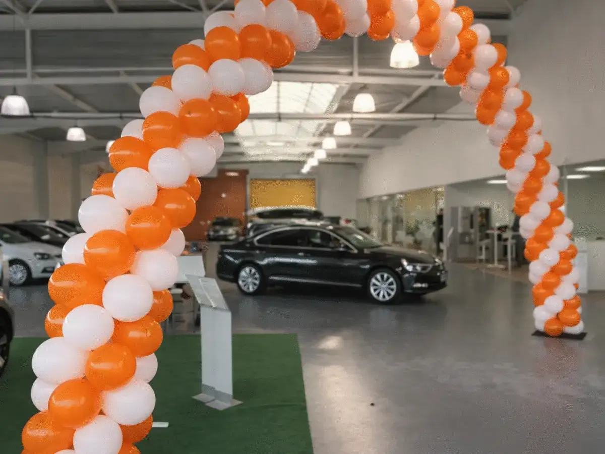 Une arche de ballons orange et blancs pour un événement spécial, peut-être un lâcher de ballons pour célébrer l'ouverture d'une concession automobile.