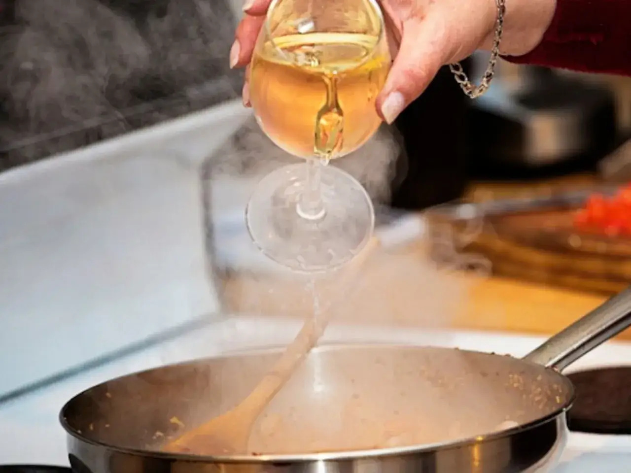 Flüssigkeit aus einem Weinglas wird in eine dampfende Pfanne gegossen. So verdunstet Alkohol beim Kochen.