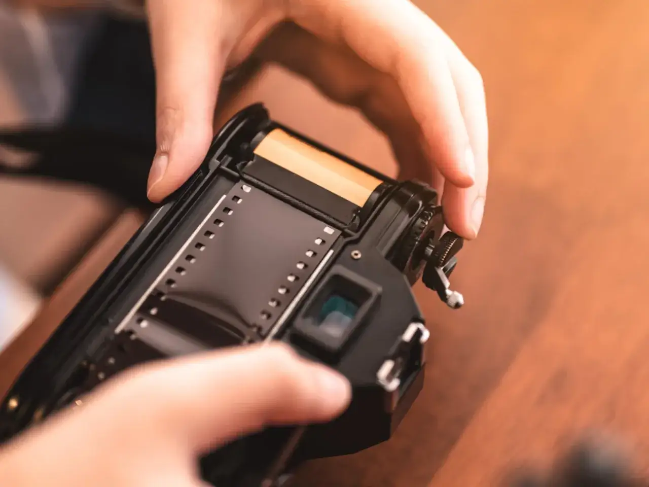 Manos insertando un carrete de pel&iacute;cula en una c&aacute;mara antigua, prepar&aacute;ndose para revelar un carrete.