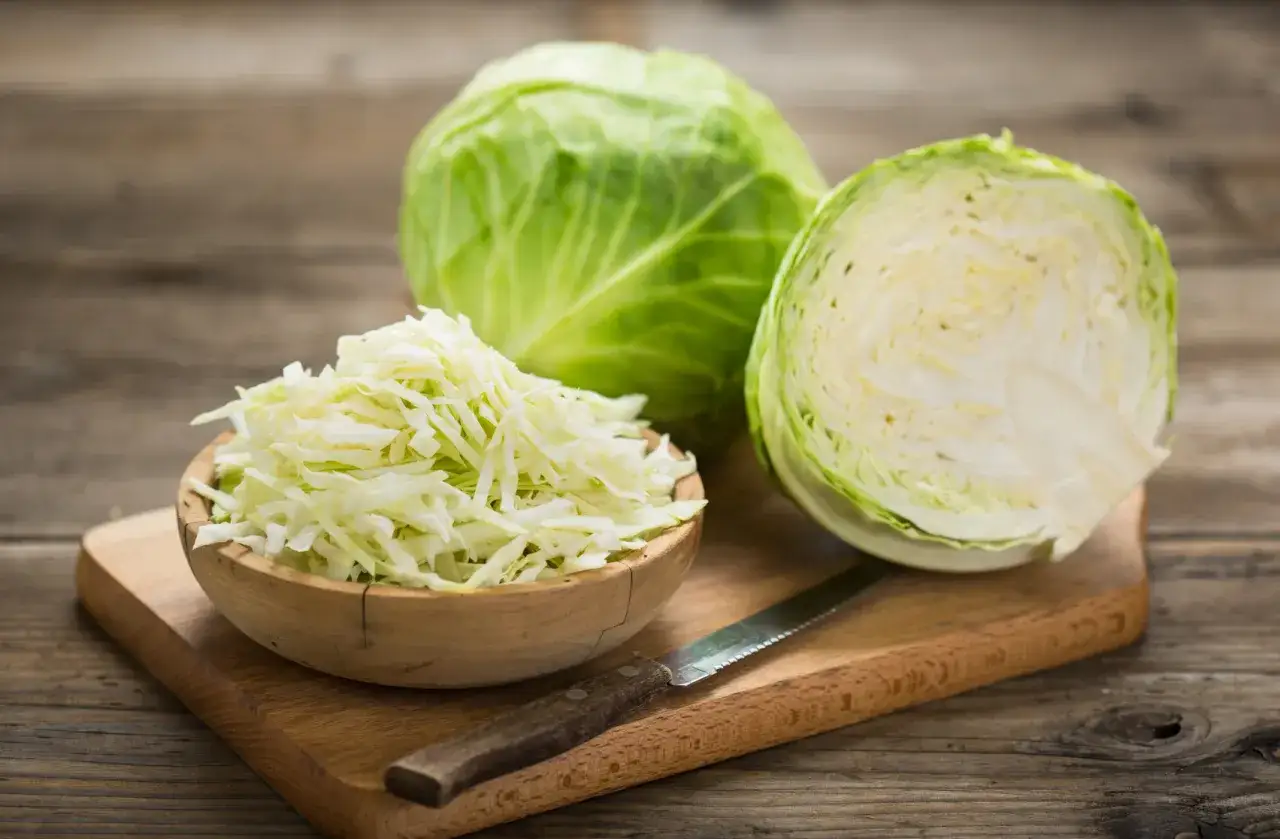 Verza tagliata finemente in una ciotola di legno, pronta per essere cucinata in padella. Accanto, una verza intera e una tagliata a metà.