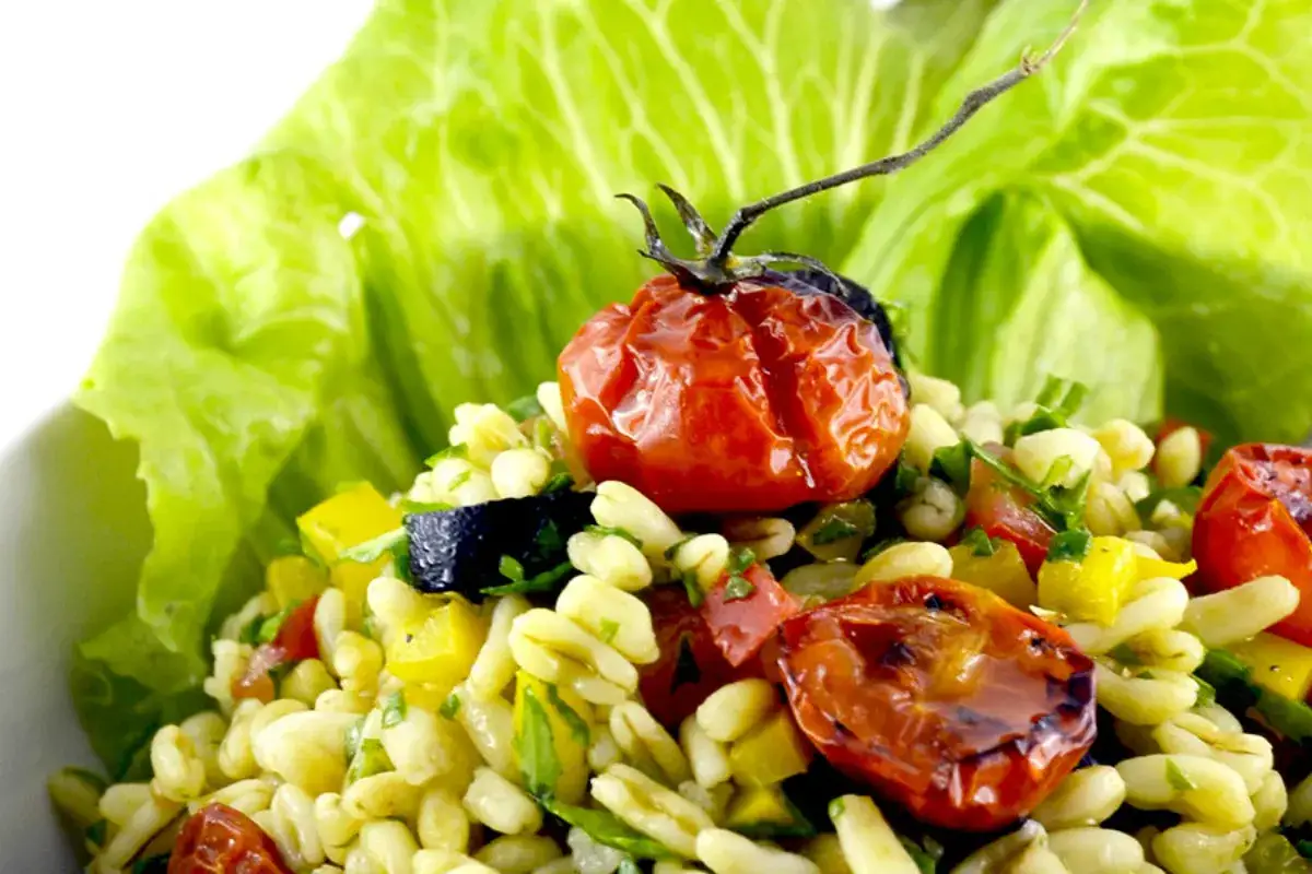 Deliziosa insalata di cereali con pomodorini confit, peperoni gialli e olive nere, guarnita con foglie di lattuga fresca.