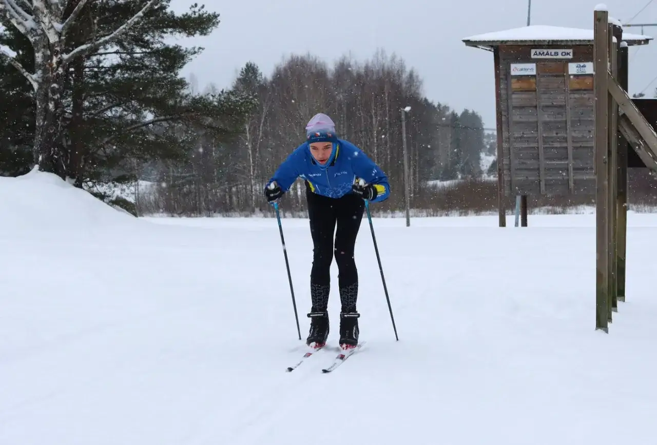 Ung skidåkare i blå jacka och svarta byxor tränar åmål skidor i snöfall.