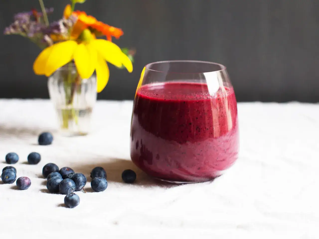 Ein Glas leuchtend roter Smoothie mit rote Bete und Blaubeeren, daneben frische Beeren und ein kleiner Blumenstrauß.