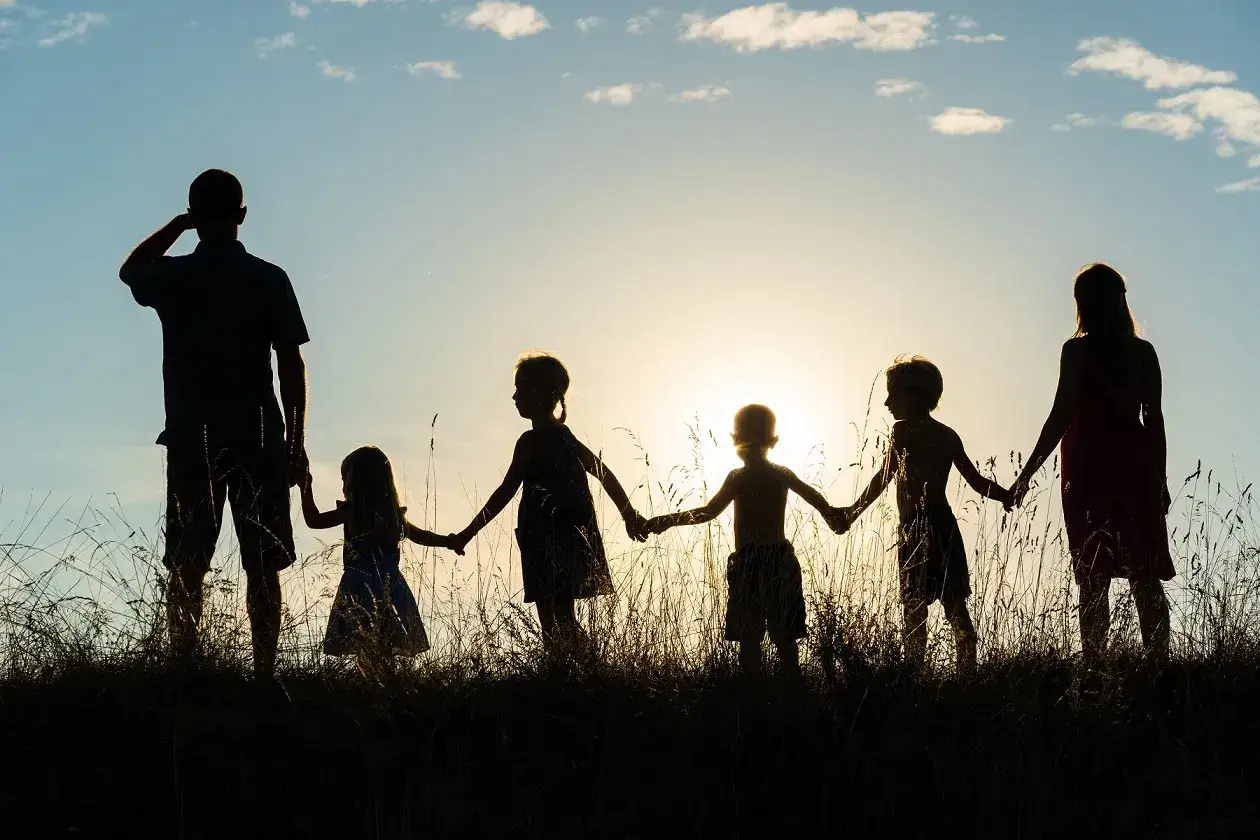 Rodzina z czwórką dzieci, mama 4 plus, trzymają się za ręce na tle zachodzącego słońca.