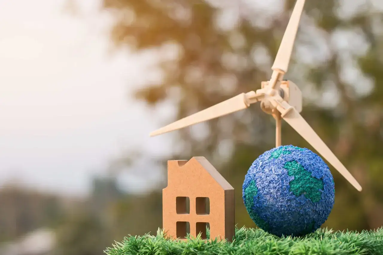 Model domu, globus i miniaturowa turbina wiatrowa na tle zieleni symbolizują czysty prąd i ekologiczne rozwiązania dla przyszłości.