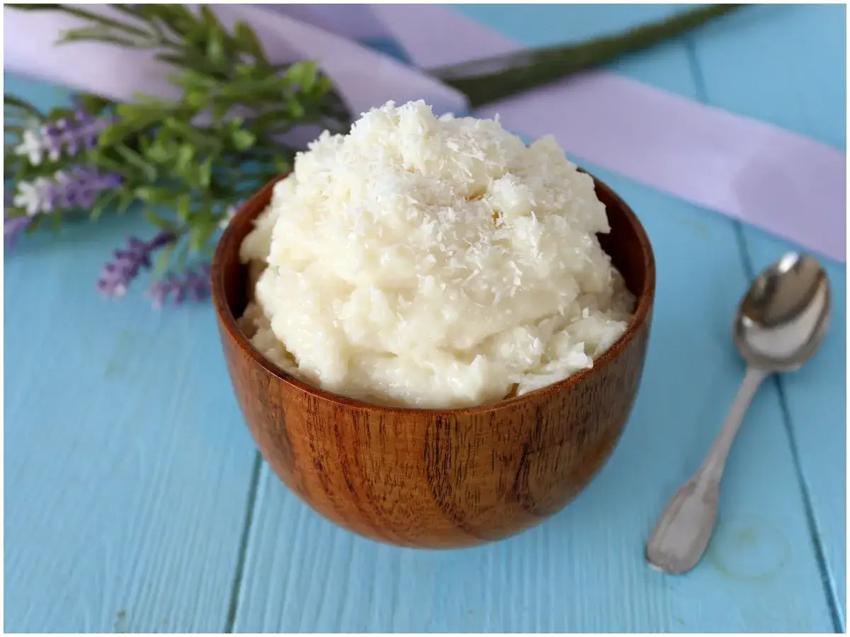 Deliziosa crema al cocco in una ciotola di legno, guarnita con cocco grattugiato. Accanto, un cucchiaino d'argento.