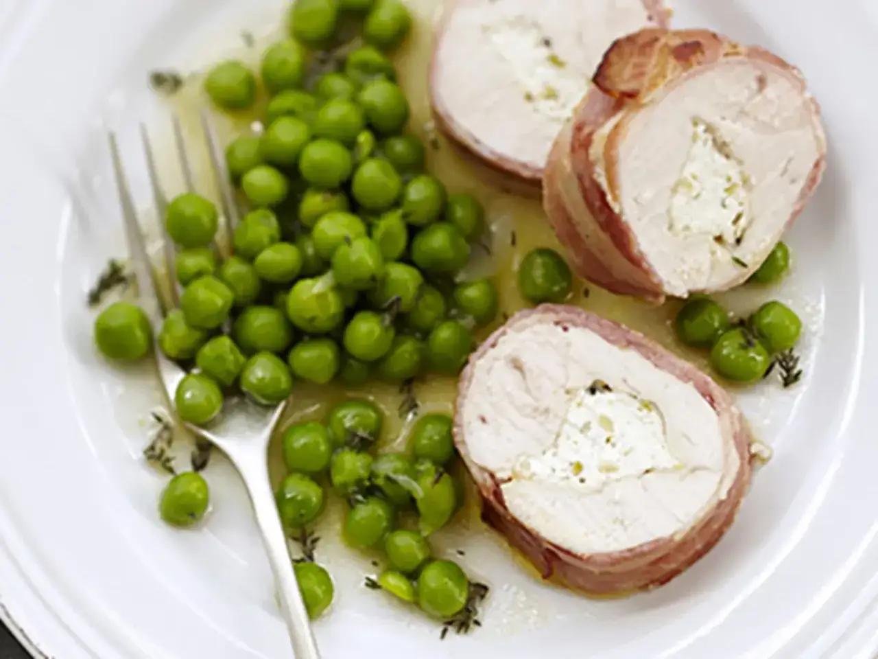 Poulet roulé au fromage blanc, enrobé de lard, servi avec des petits pois frais. Un délice !