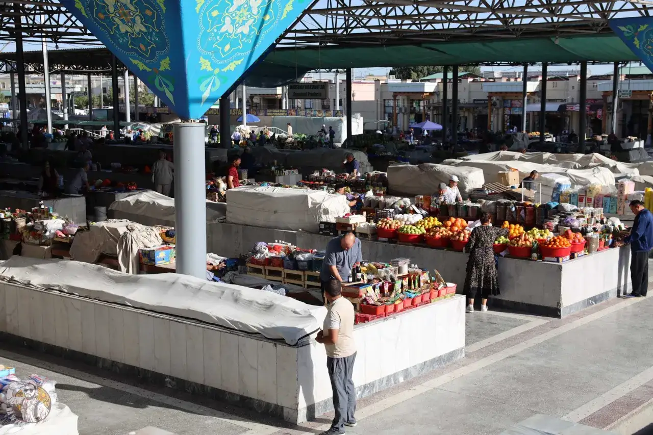 Tętniący życiem targ w Uzbekistanie, gdzie sprzedawcy oferują świeże owoce i warzywa. Ludzie spokojnie spacerują, co sugeruje, że Uzbekistan jest bezpieczny.