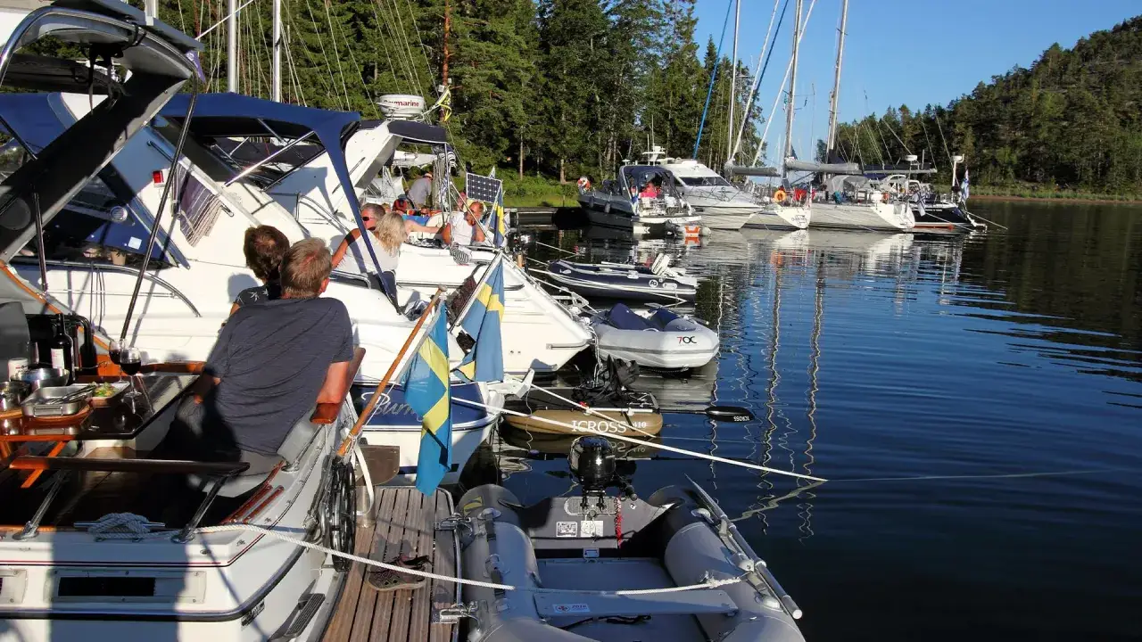 Solig dag i hamnen med flera segelb&aring;tar och motorb&aring;tar. Ett b&aring;tk&ouml;k syns p&aring; en av b&aring;tarna, med mat och dryck redo.