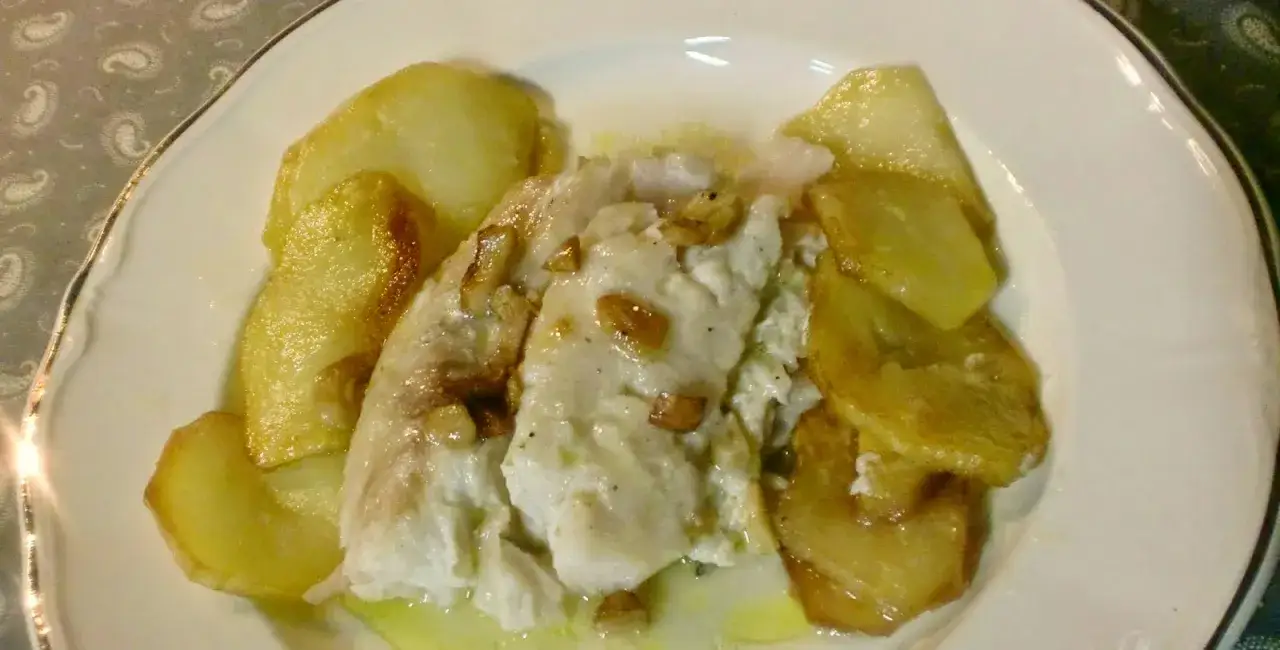 Merluza a la bilbaina con patatas doradas y ajo laminado, un plato tradicional y delicioso.