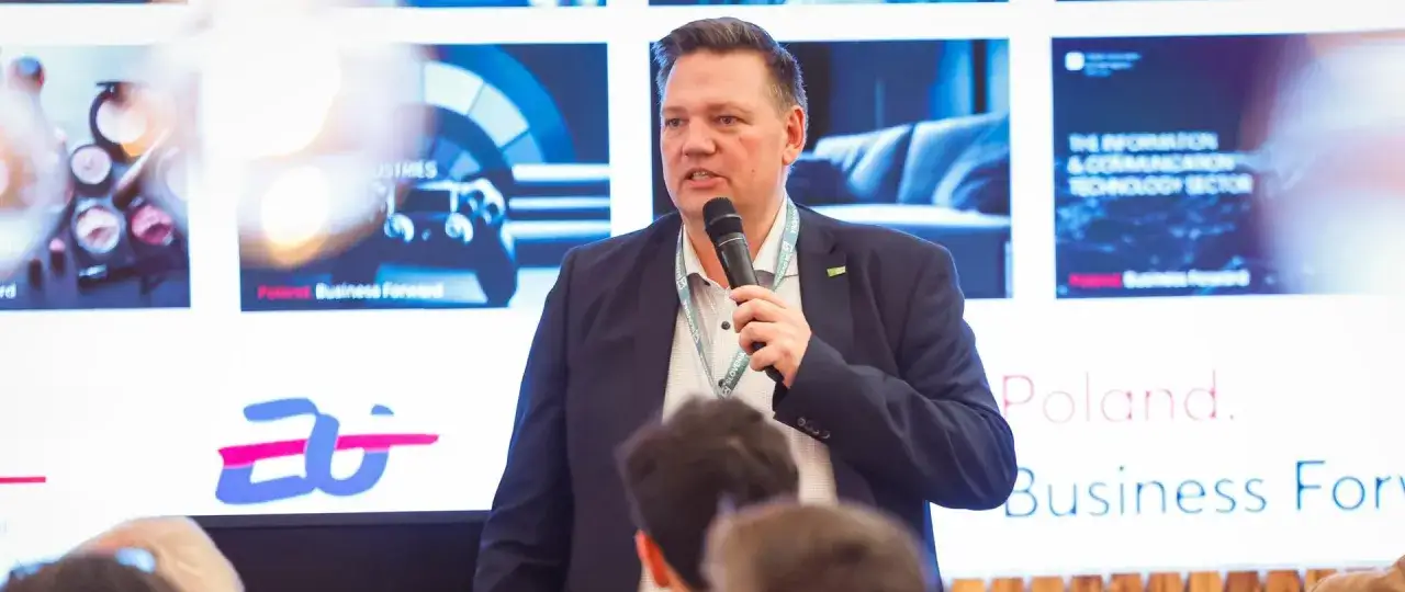 Mężczyzna przemawia na konferencji, gdzie widnieje napis