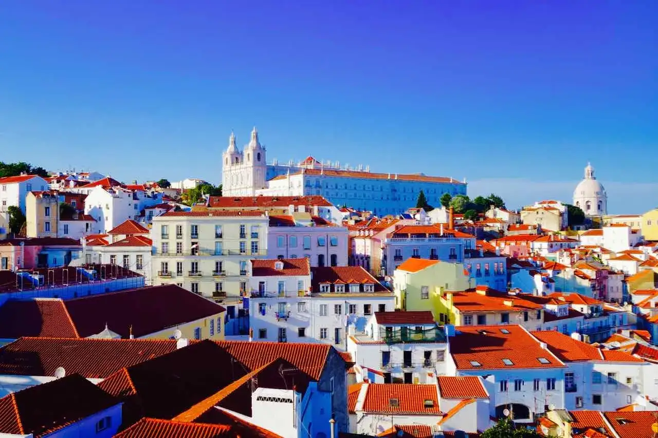 Bunte Häuser mit roten Ziegeldächern unter blauem Himmel. Ein Blick auf Lissabon, der Lust auf weitere Lissabon Geheimtipps macht.