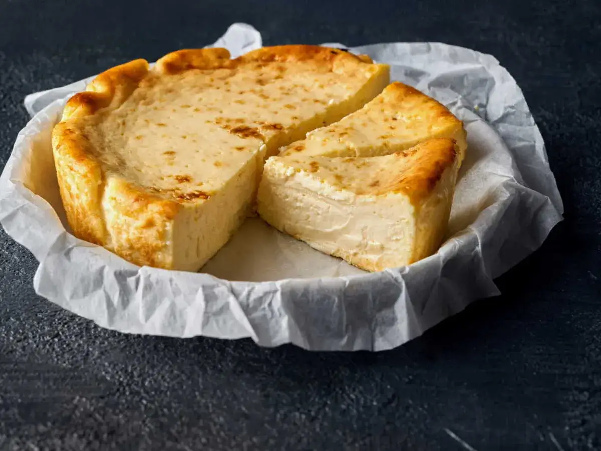 Un fiadone doré, inspiré de la recette Les Carnets de Julie, est coupé en parts sur du papier sulfurisé.