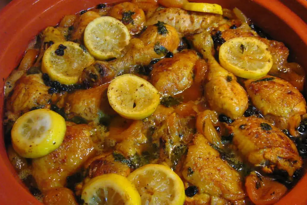 Un plat de tajine poulet citron, avec des morceaux de poulet dorés, des rondelles de citron, des abricots secs et des olives noires, le tout mijoté dans une sauce savoureuse.