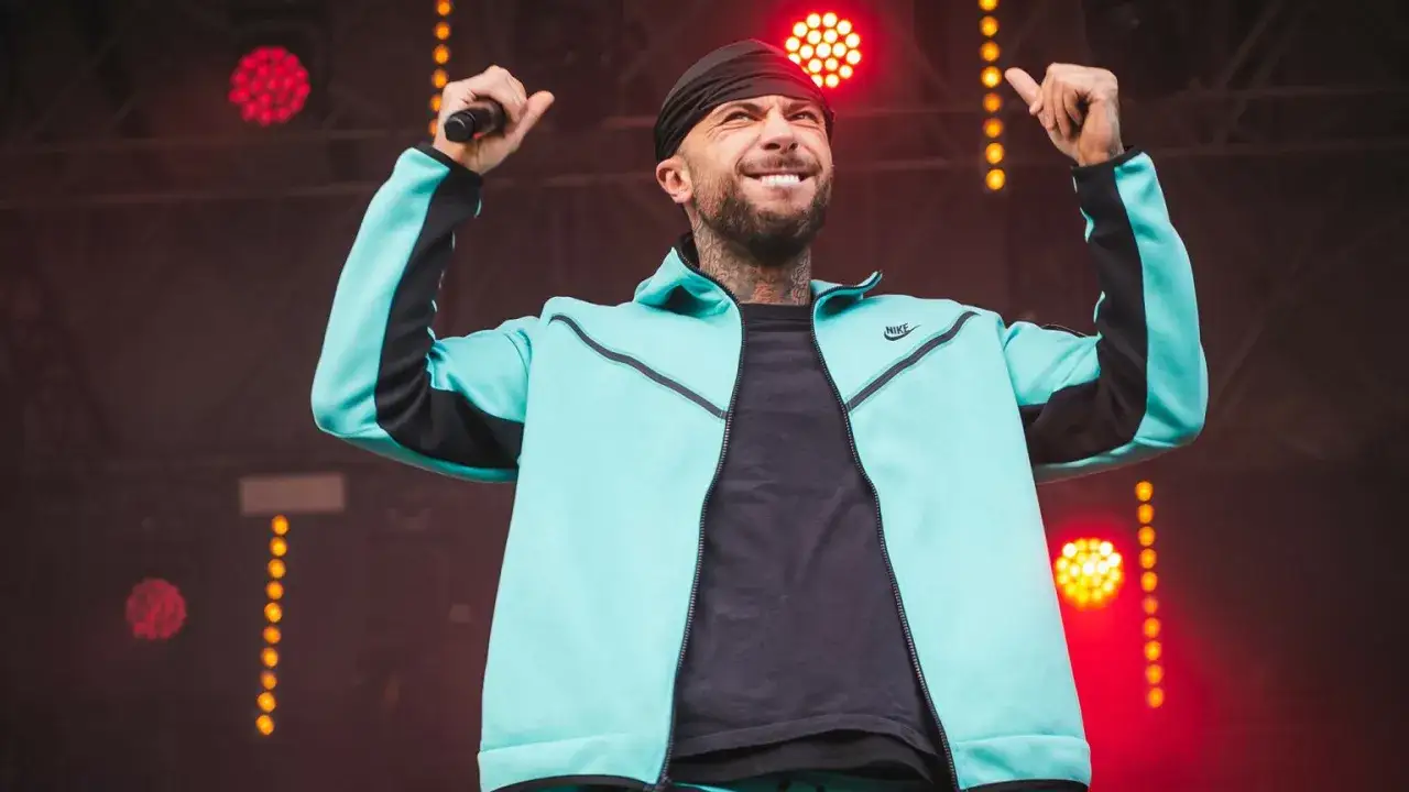Malik Montana we Wrocławiu na scenie, w turkusowej bluzie Nike, z mikrofonem w dłoni, rozgrzewa publiczność.