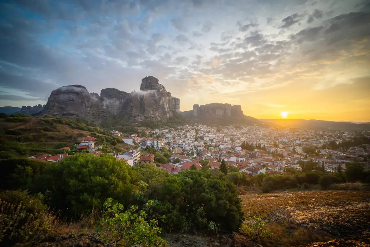 Solnedgång över Meteora, Grekland. Imponerande klippformationer reser sig över en stad med röda tak.