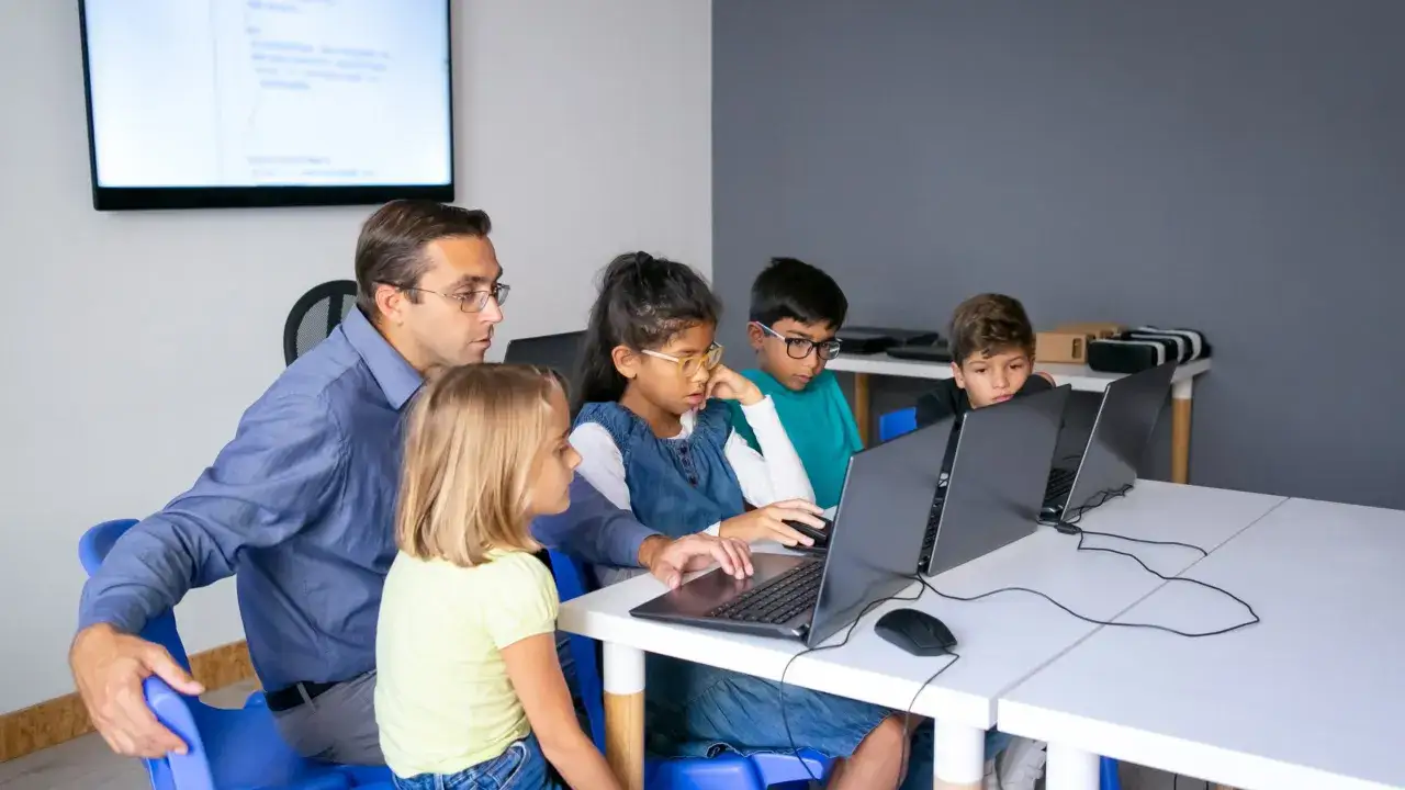 Lehrer unterst&uuml;tzt Kinder beim **hybrid unterricht** an Laptops.