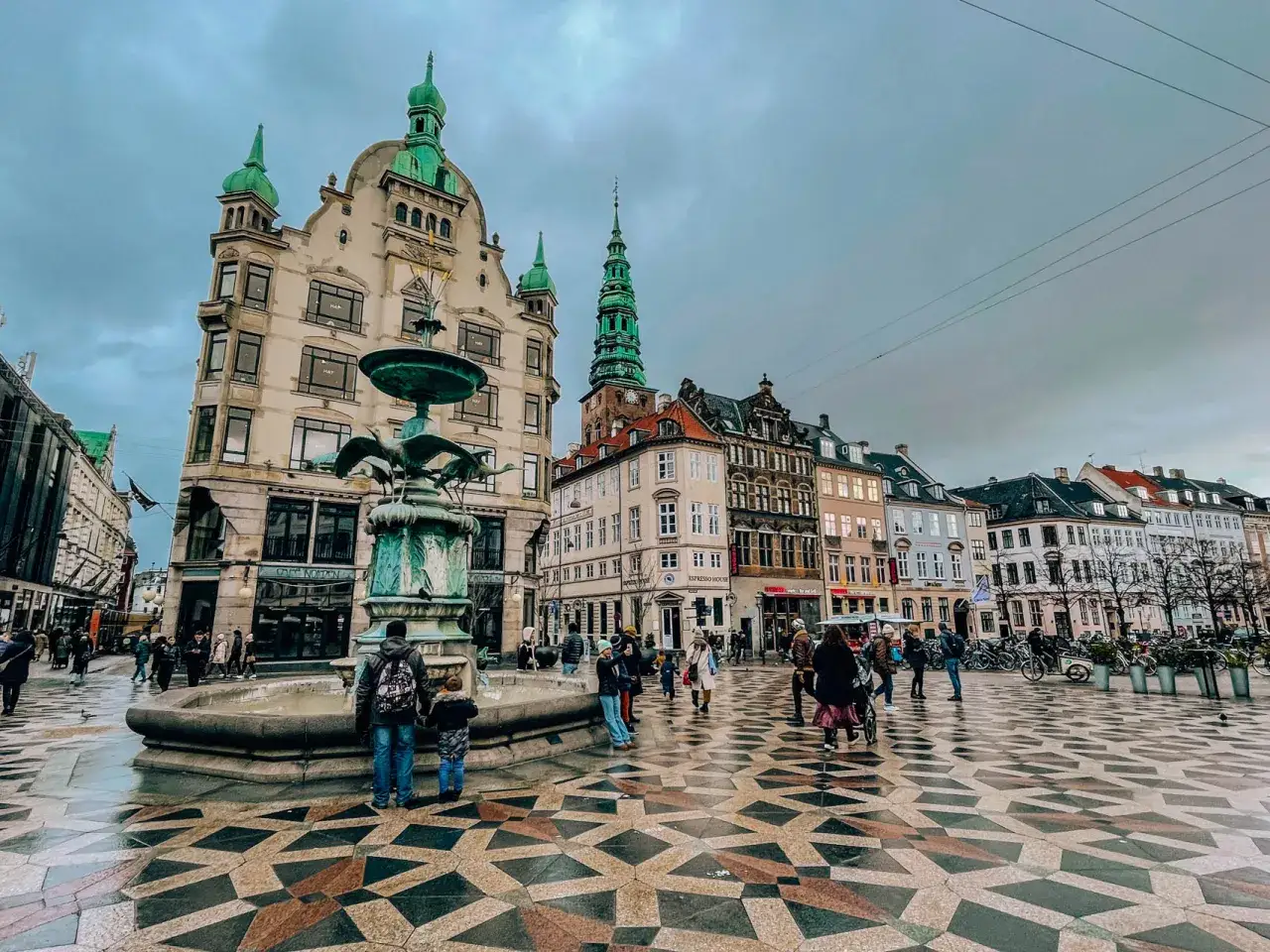 Tłoczny plac w Kopenhadze z fontanną i ludźmi. Warto sprawdzić ceny w Kopenhadze, bo są wysokie.