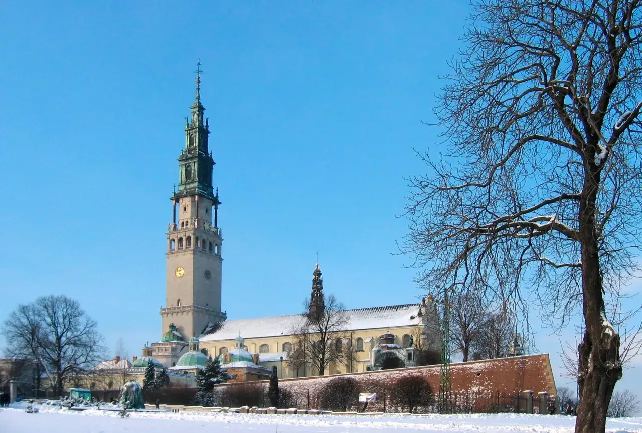 Zimowy dzień w Sanktuarium Matki Bożej Częstochowskiej. Śnieg otula dziedziniec, a wieża klasztoru góruje nad krajobrazem.