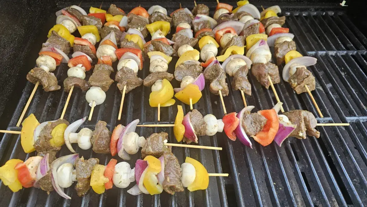 Brochettes de bœuf marinées prêtes à griller, garnies de poivrons colorés, d'oignons rouges et de champignons sur un barbecue.