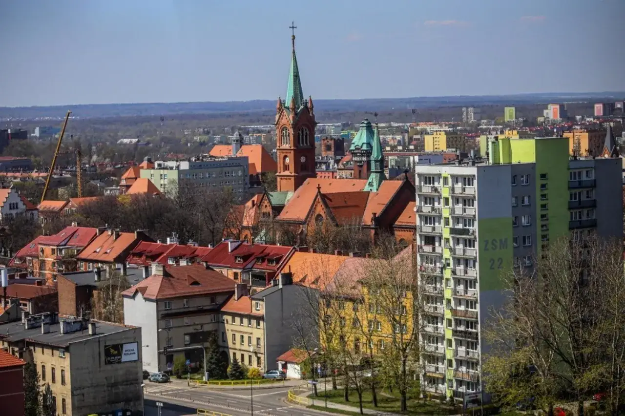 Widok na miasto z wieżą ciśnień w Zabrzu w tle. Widać kościół, budynki mieszkalne i drzewa.