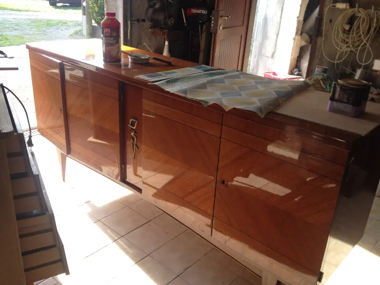 Pr&eacute;paration pour poncer un meuble vernis : un d&eacute;capant et des outils sont pr&ecirc;ts sur le buffet en bois.