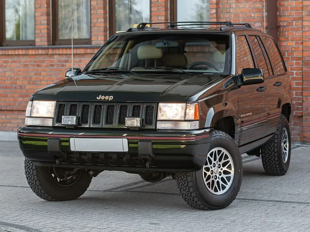 Ciemnozielony Jeep Grand Cherokee ZJ z lat 90. stoi przed ceglanym budynkiem.