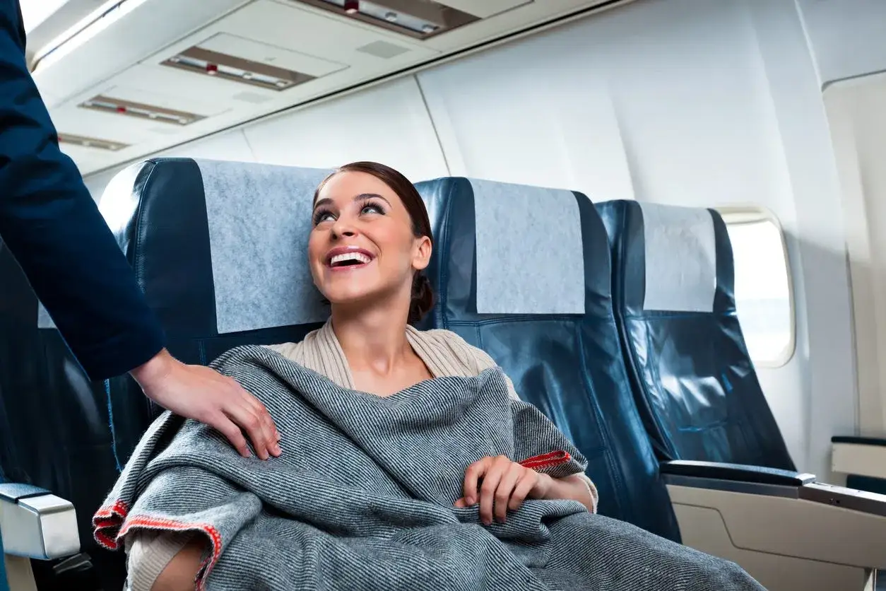 Assistente di volo offre una coperta a una passeggera sorridente. Un'immagine che ispira a capire come diventare assistente di volo.