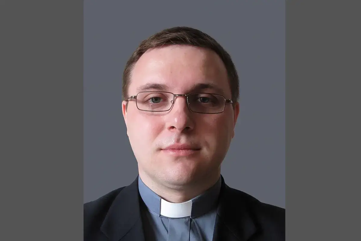 Młody mężczyzna w okularach, ubrany w sutannę i marynarkę. To najmłodszy biskup w Polsce, który z powagą patrzy w obiektyw.