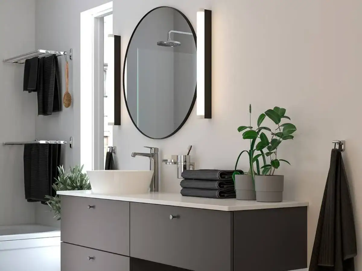 Moderno lavabo con grifer&iacute;a cromada, espejo ovalado y toallas negras. Un toque de verde con plantas. Ideal para una reforma ba&ntilde;o peque&ntilde;o.