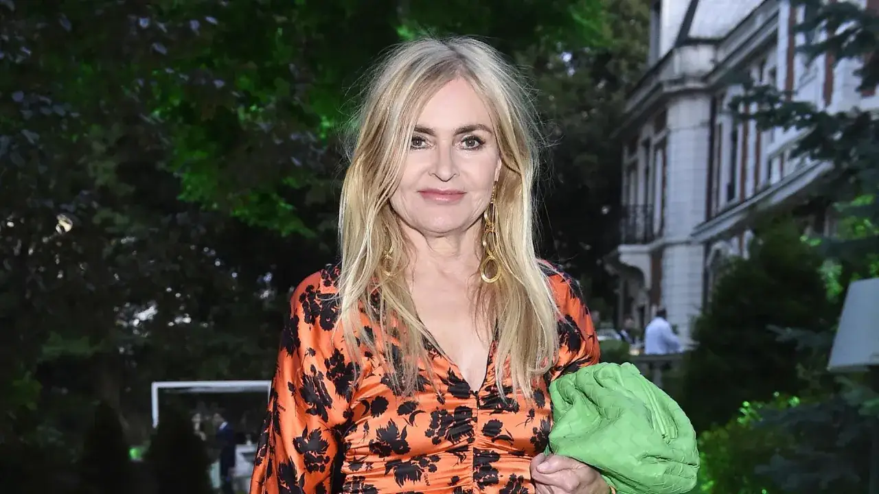 Monika Olejnik, której wiek dodaje jej uroku, w pomarańczowej sukience w czarne wzory i zielonej torebce.