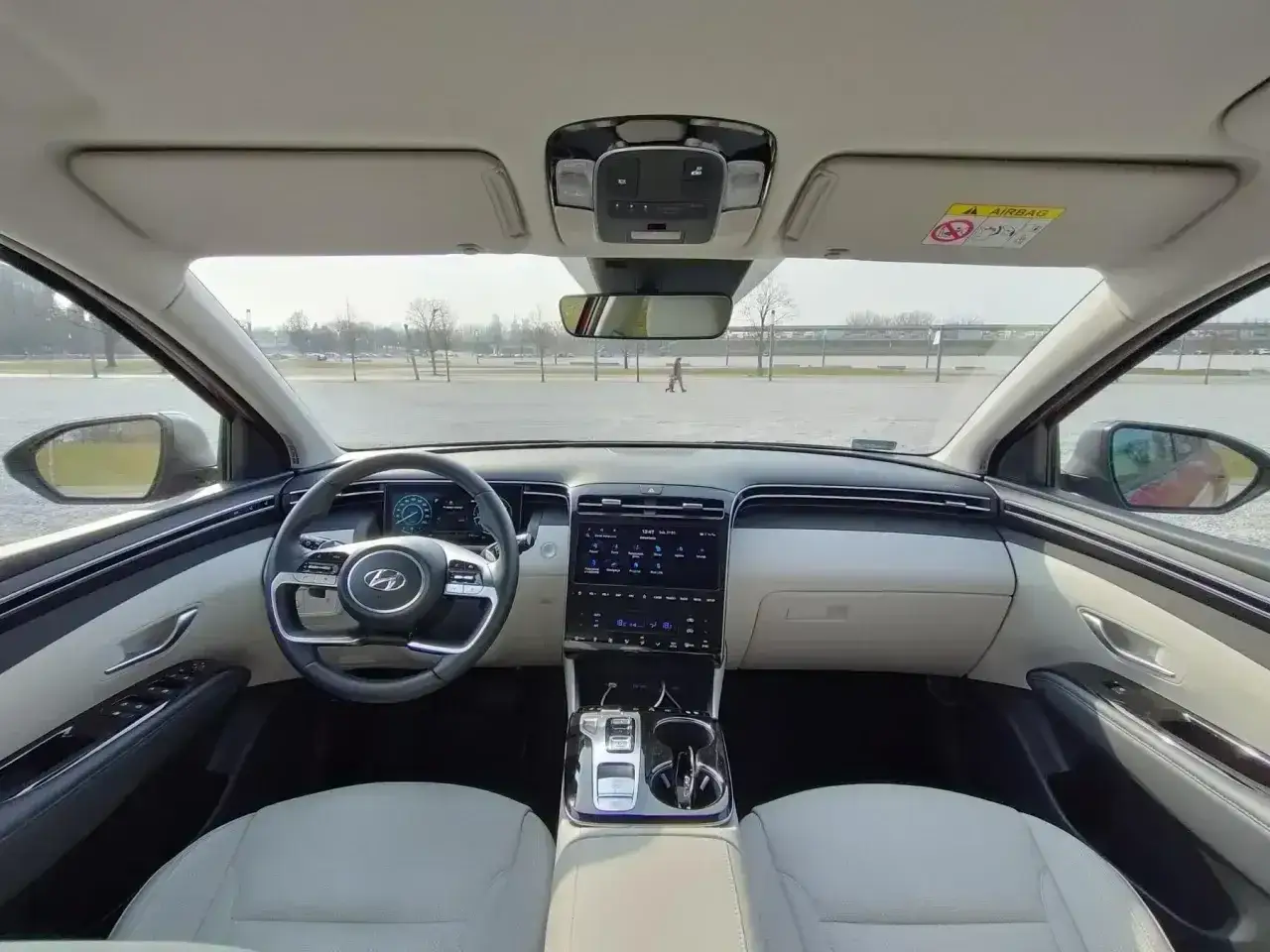 Wnętrze Hyundai Tucson 2024: nowoczesny kokpit z ekranami, jasne fotele i kierownica.