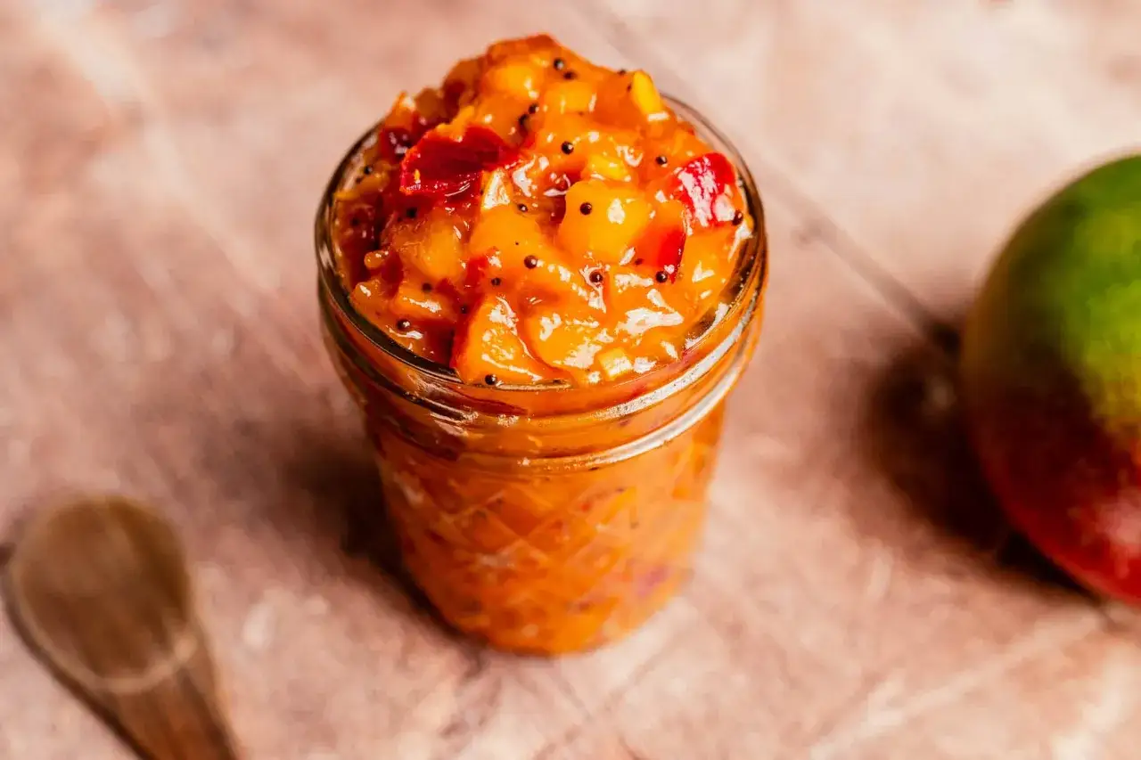 En burk med hemgjord mango chutney, perfekt för ditt nästa mango chutney recept. En mango syns till höger.