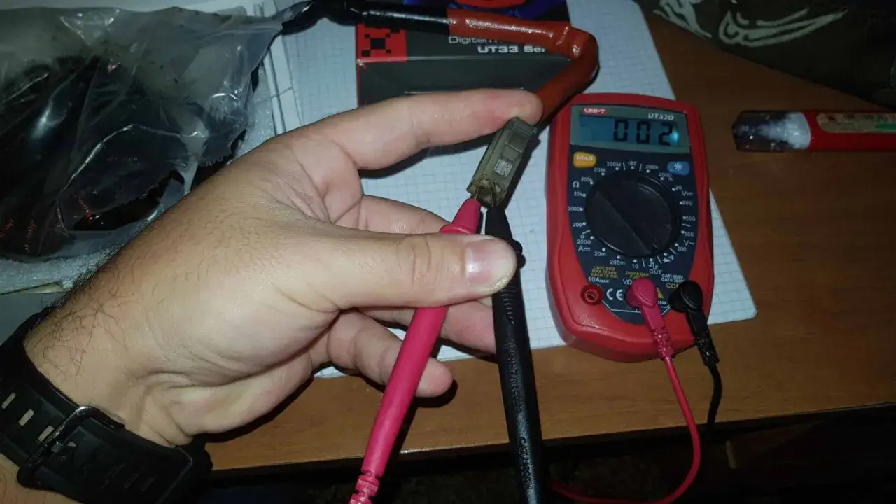 Test del regolatore di tensione moto con multimetro. La mano tiene i puntali per misurare la resistenza.