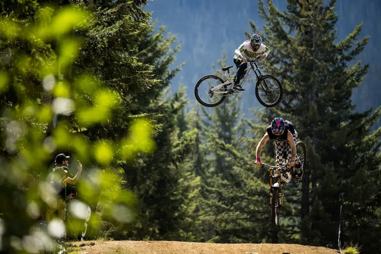 Tomas Lemoine soars through the air on his bike, performing an epic jump against a backdrop of lush green trees and a clear blue sky.