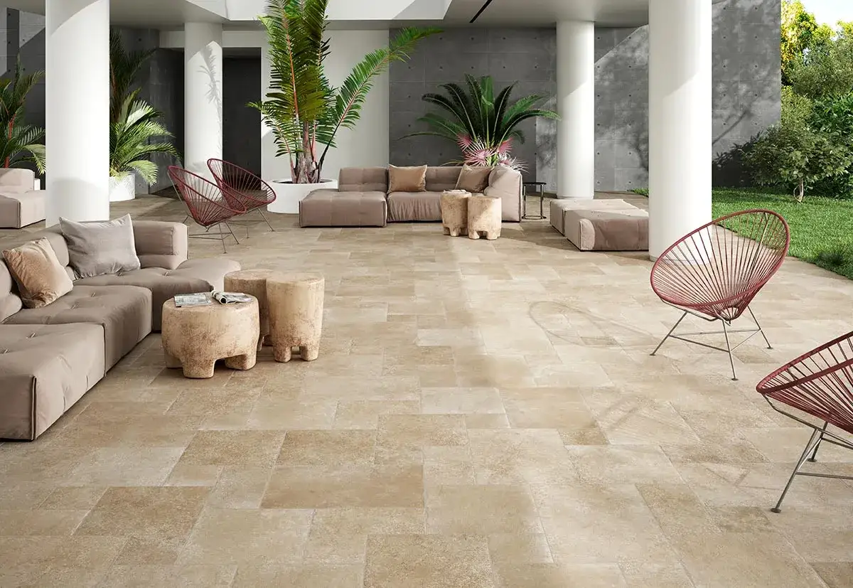 Amplia terraza exterior con suelo de baldosas de piedra natural, sofás modulares, sillas rojas y vegetación exuberante.