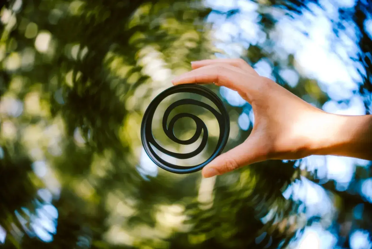 A hand holds a circular filter with a swirly bokeh pattern, creating a vortex of light and color.