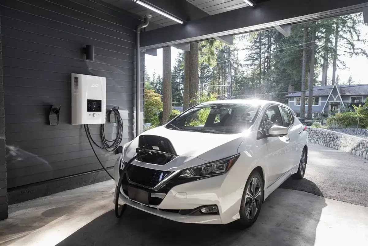 Une voiture électrique blanche se recharge à domicile. Le système de charge est fixé au mur, prêt pour l'installation. L'impôt sur ce type d'équipement est un sujet d'actualité.