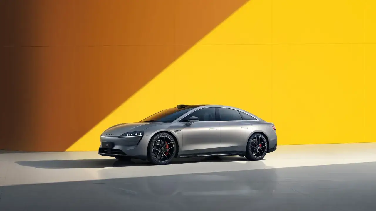 Coche el&eacute;ctrico gris, un modelo de **coche Huawei** con dise&ntilde;o futurista, aparcado frente a una pared amarilla con luz solar.