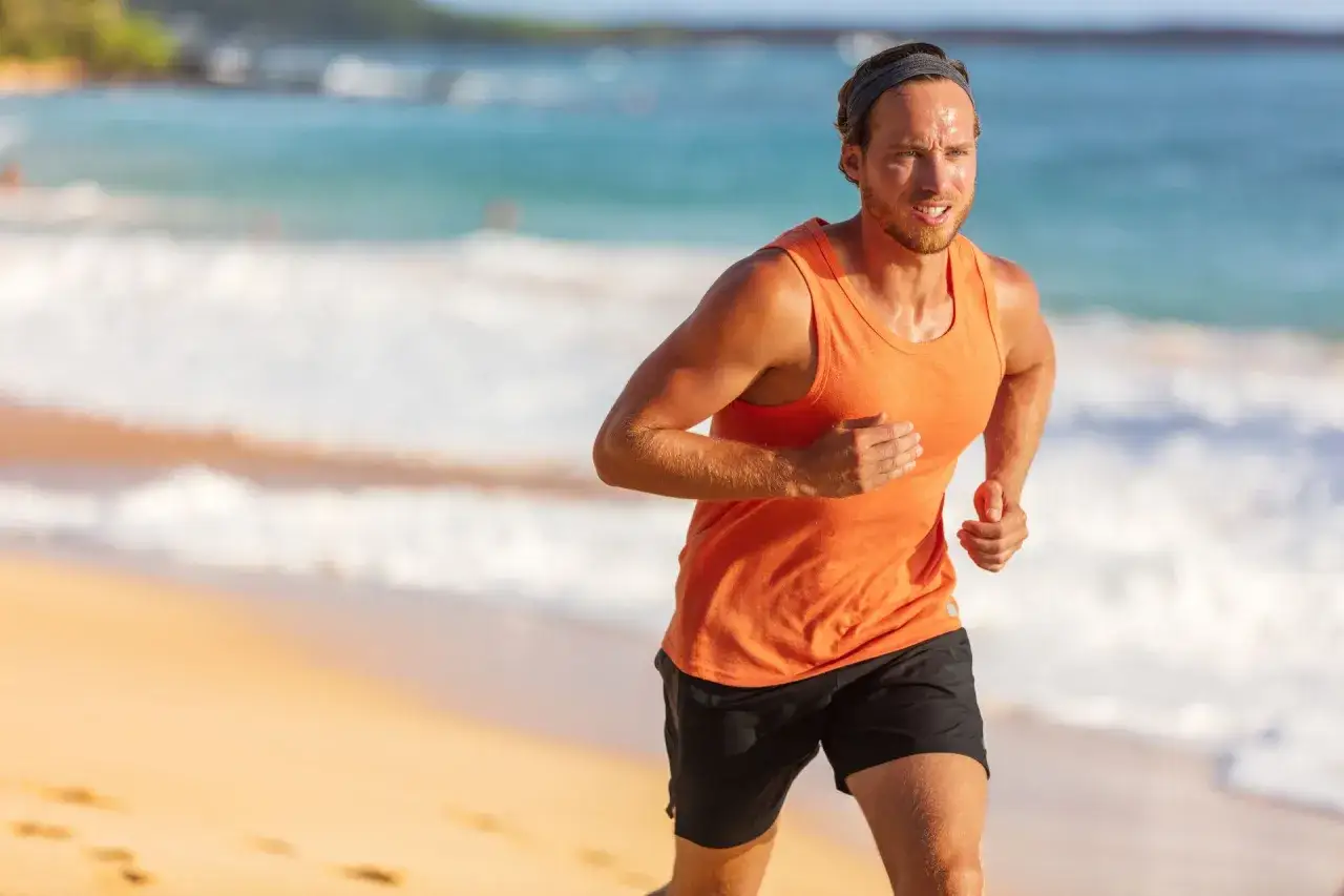 Mann joggt bei 30 Grad am Strand. Schwei&szlig;perlen auf der Stirn, die Wellen rauschen im Hintergrund.