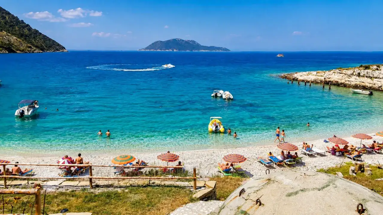 Słoneczna plaża Karaburun z turkusową wodą, łodziami i ludźmi odpoczywającymi pod parasolami.