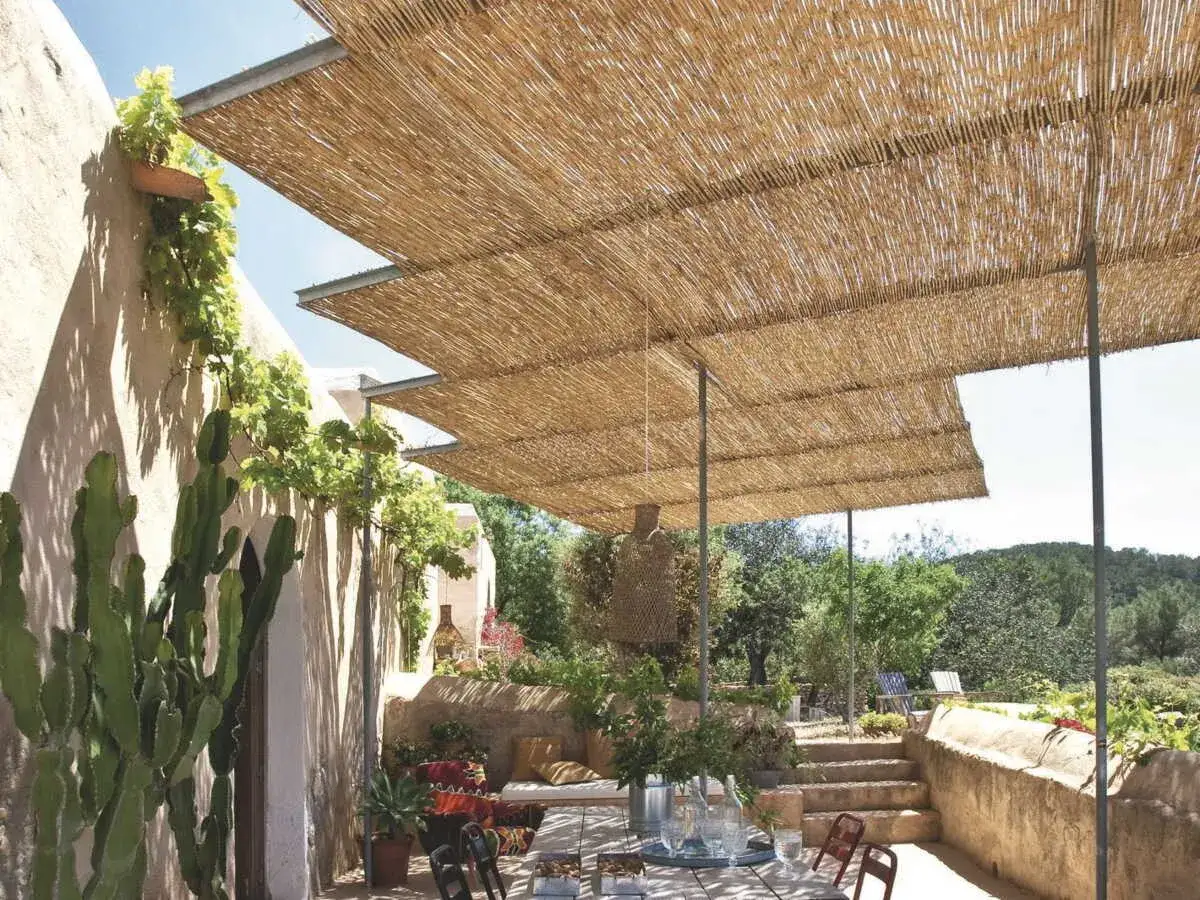 Une **pergola bois canisse** offre une ombre naturelle et chaleureuse &agrave; cette terrasse m&eacute;diterran&eacute;enne, orn&eacute;e de cactus et de v&eacute;g&eacute;tation luxuriante.