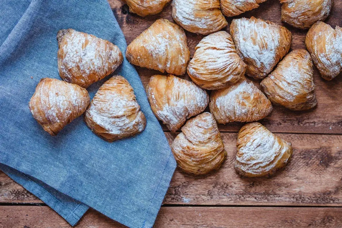 Sfogliatelle, un delizioso cibo tipico napoletano, cosparse di zucchero a velo su un tavolo di legno e un tovagliolo blu.