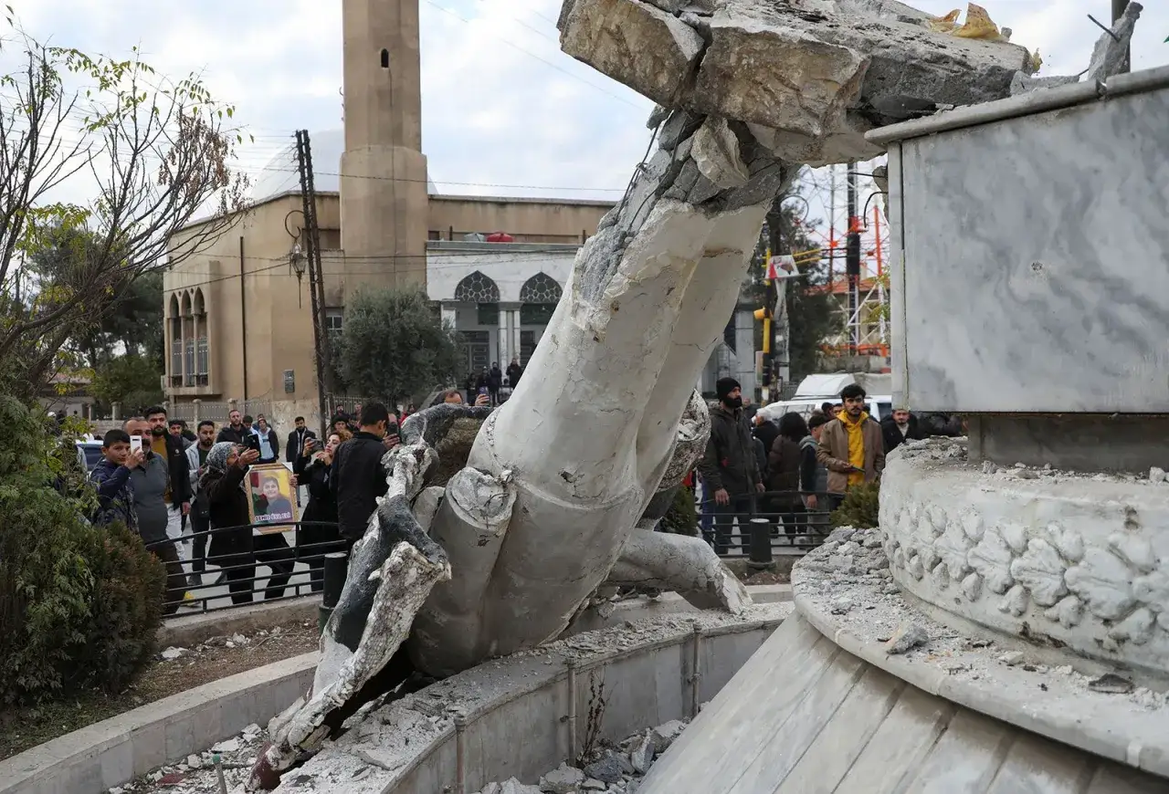 En grupp m&auml;nniskor samlas runt en f&ouml;rst&ouml;rd staty i Syrien. En kvinna h&aring;ller upp en bild p&aring; ett barn. Detta &auml;r en del av fakta om Syrien.