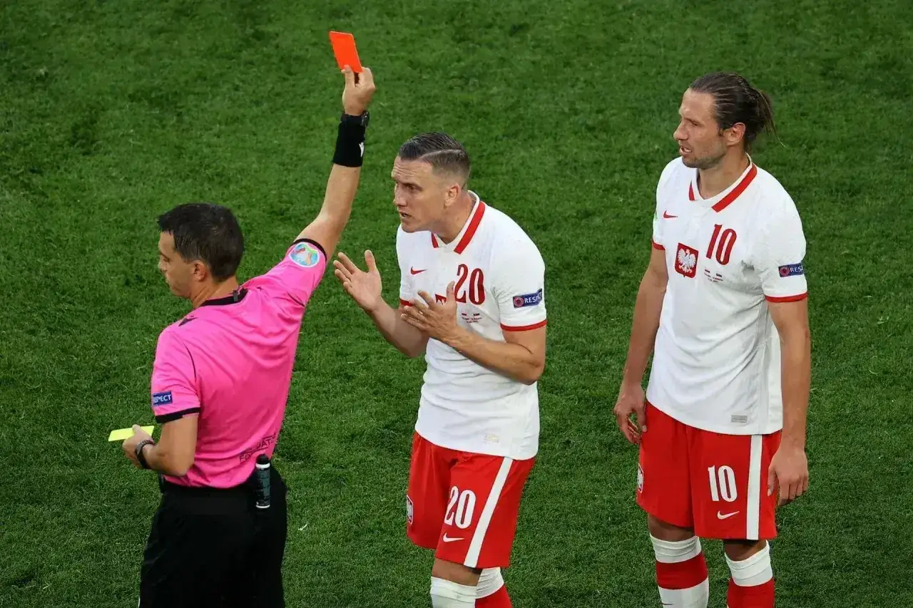 Sędzia pokazuje czerwoną kartkę, co oznacza koniec gry dla zawodnika.