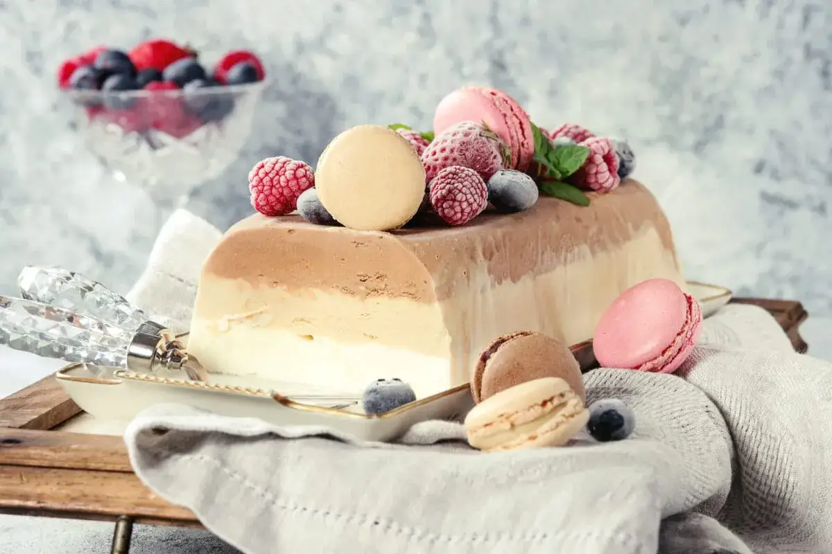 Wykwintny tort lodowy w trzech kolorach, ozdobiony malinami, borówkami i makaronikami. Idealny deser na letnie popołudnie.