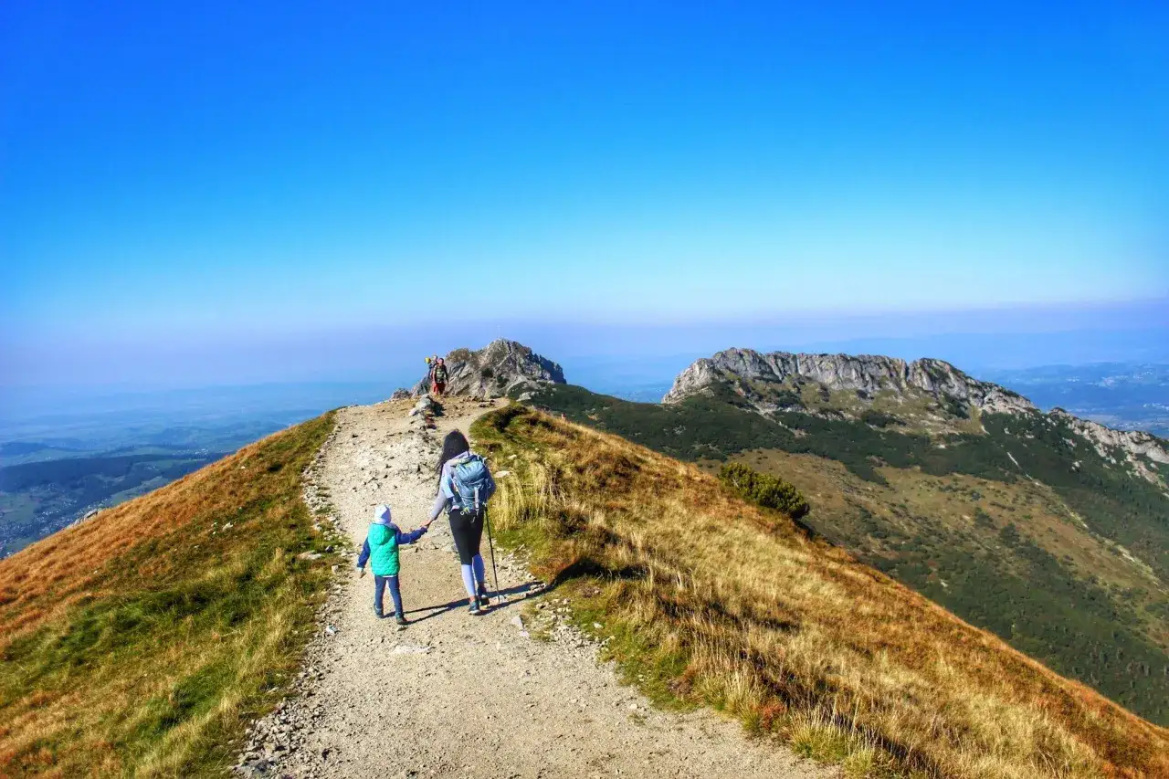 Mama z dzieckiem idą szlakiem na Giewont. Piękny widok na Tatry i błękitne niebo.